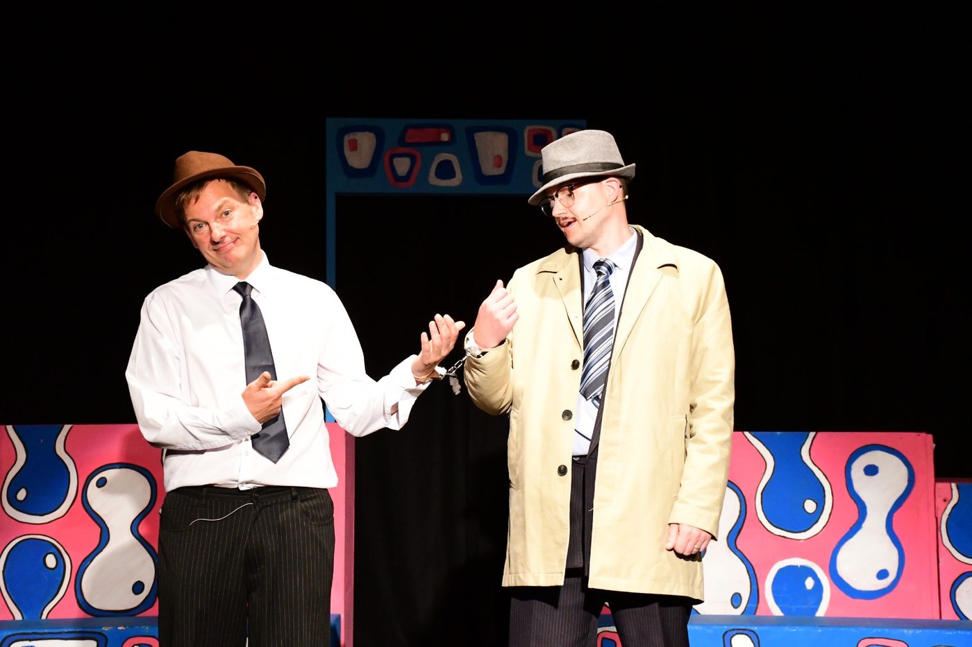 Two performers handcuffed together, one pointing at the cuffs in mock outrage