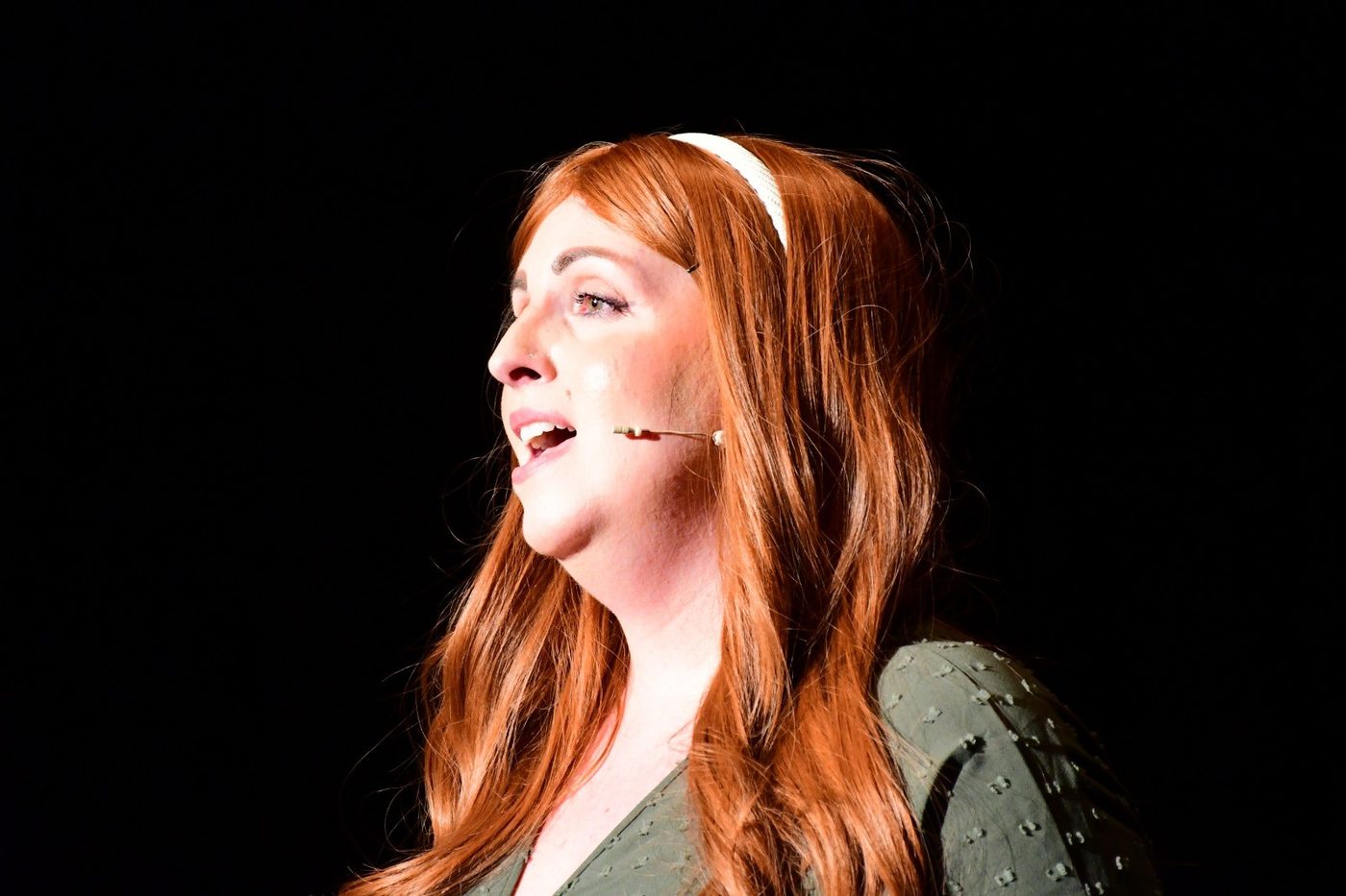 A singer in profile under a single spotlight, mid-song